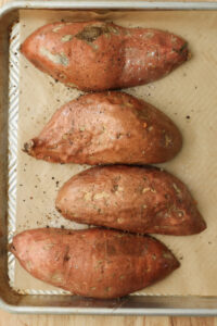 The sweet potatoes are cut side down and are ready to roast on a cookie sheet.