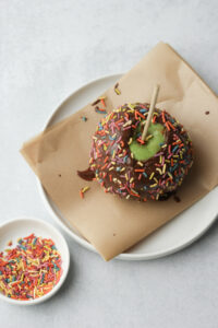 The caramel apple has been sprinkled with colored sprinkles.