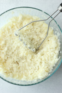 Mashing the potatoes with a potato masher.