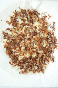 The crispy shallots are cooling off on a paper towel.