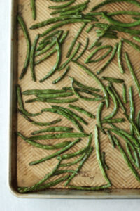The green beans are on a lined baking sheet and have just been roasted.