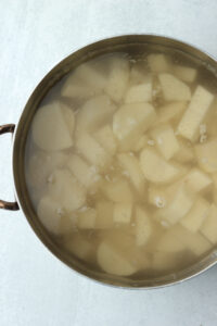 The potato cubes are in a large pot with salted water and are ready to be boiled.