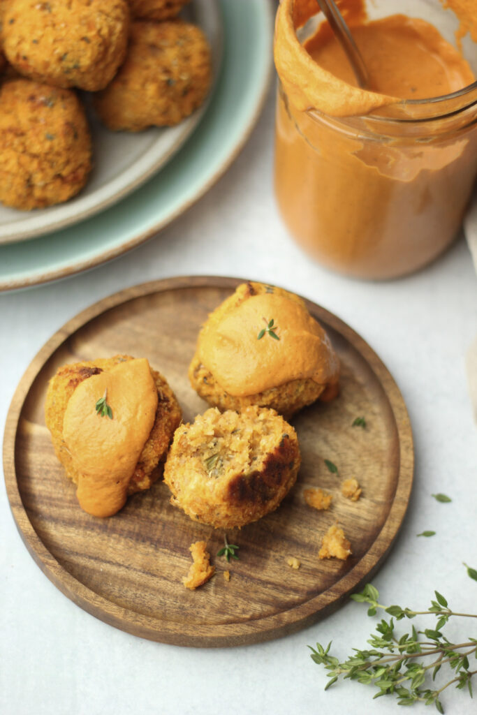 The sweet potato balls are on a wooden plate, drizzlds with bell pepper sauce, and are ready to eat.