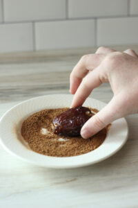 The stuffed dates are being pressed into the cinnamon and sugar mixture. 