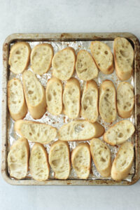The baguette slices have been toasted on a pan.
