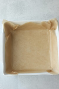 An 8x8 casserole dish has been lined with parchment paper.