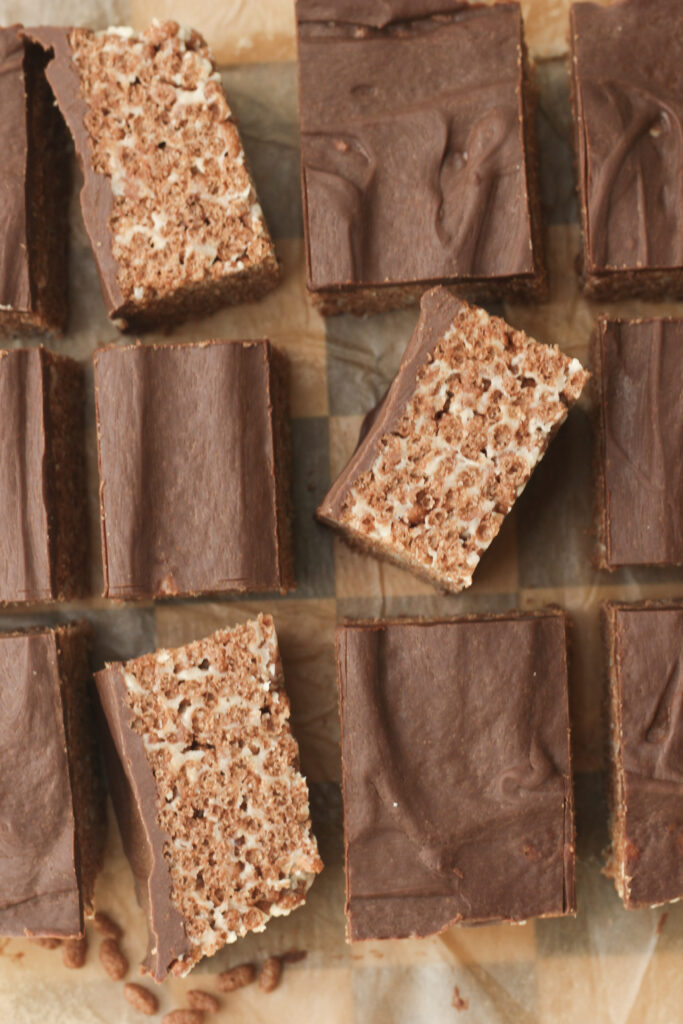 The rice krispie treats have been cut into squares and are lying on a cutting board.