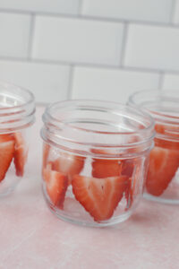 Thinly sliced strawberries have been pressed in a circle inside of each mason jar.