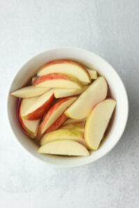 The apple slices are soaking in water and lemon juice in a small bowl.