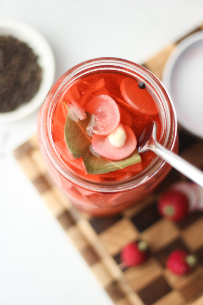 An overhead, up-close picture of the finished pickled radishes in a large jar.