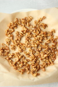 The warm candied walnuts have been transferred to a parchment paper-lined plate to cool.