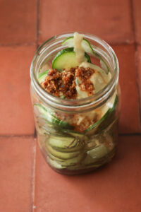 All of the sauce ingredients have been added to the jar of sliced cucumbers.