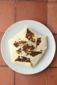 The Crunchwrap has been folded into a pinwheel shape and toasted in a pan until golden brown.
