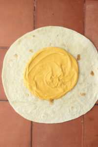 The cashew sauce has been spread into the center of a large tortilla.