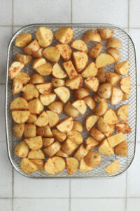 The seasoned potatoes have been spread out in an even layer in an air fryer basket.