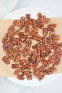 The warm pecans are cooling on a lined plate.