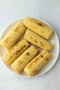 The corn has been grilled and placed on a large white plate.