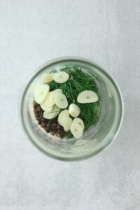 The garlic, dill, peppercorns, mustard seeds, and salt have been added to the bottom of a mason jar.