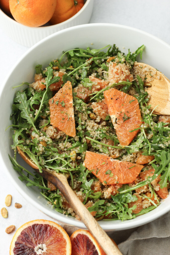 Citrus quinoa salad with arugula, mint, pistachios, and fresh oranges in a white serving bowl.