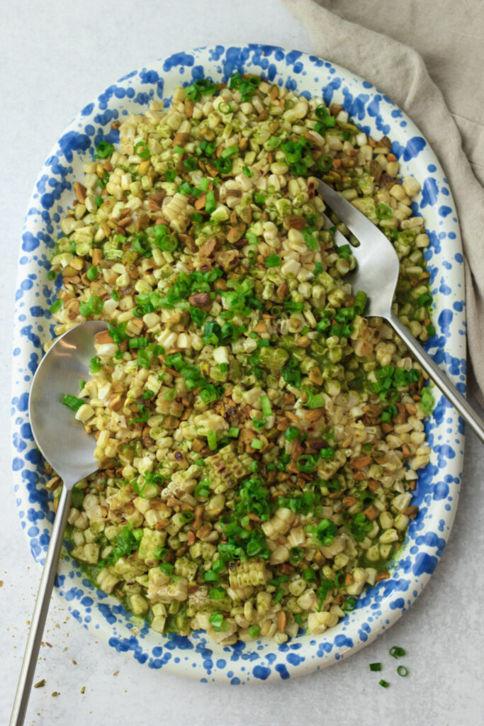 Grilled corn salad with pistachios and fresh herb dressing on a blue serving platter.