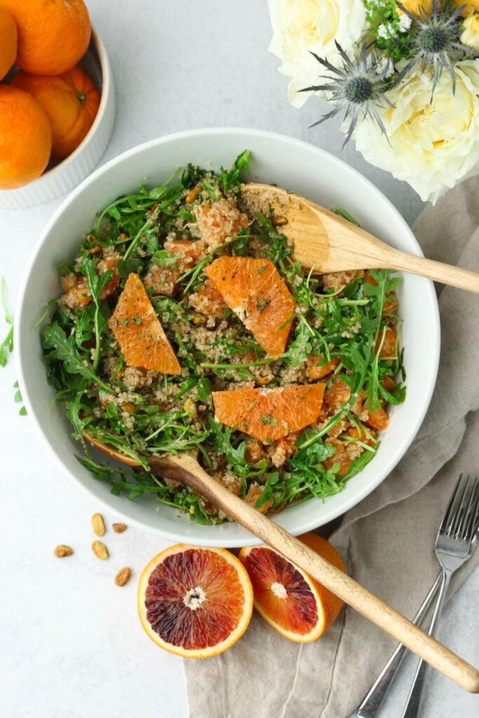 The Citrus Quinoa Salad with Arugula has been tossed with wooden serving spoons and is ready to eat.