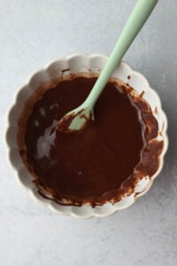 The chocolate chips and coconut oil have been melted together in a small white bowl until smooth and creamy.