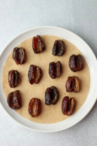 All the Medjool dates have been pitted and opened and are on a parchment-paper-lined plate.