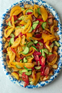 The tomatoes and cucumbers have been poured over the toasted bread cubes on a platter.