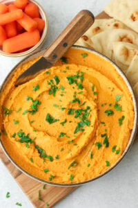 The roasted carrot and garlic hummus has been transferred to a bowl and drizzled with olive oil and psrinkles with parsely.