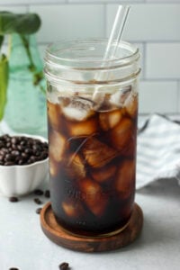 The iced coffee has been poured over ice in a large, clear mason jar cup.