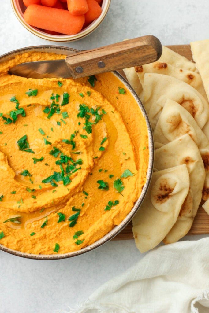 The hummus is plated with slices of pita bread for dipping.