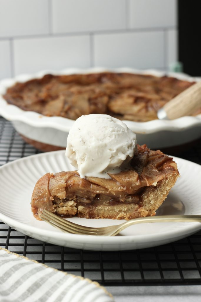 A slice of vegan apple pie topped with a scoop of vegan vailla ice cream.