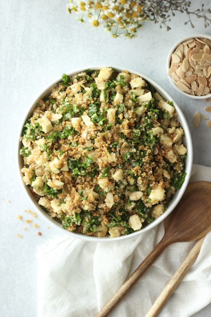 The crunchy quinoa apple salad is plated in a white salad bowl with sliced almonds on the side.