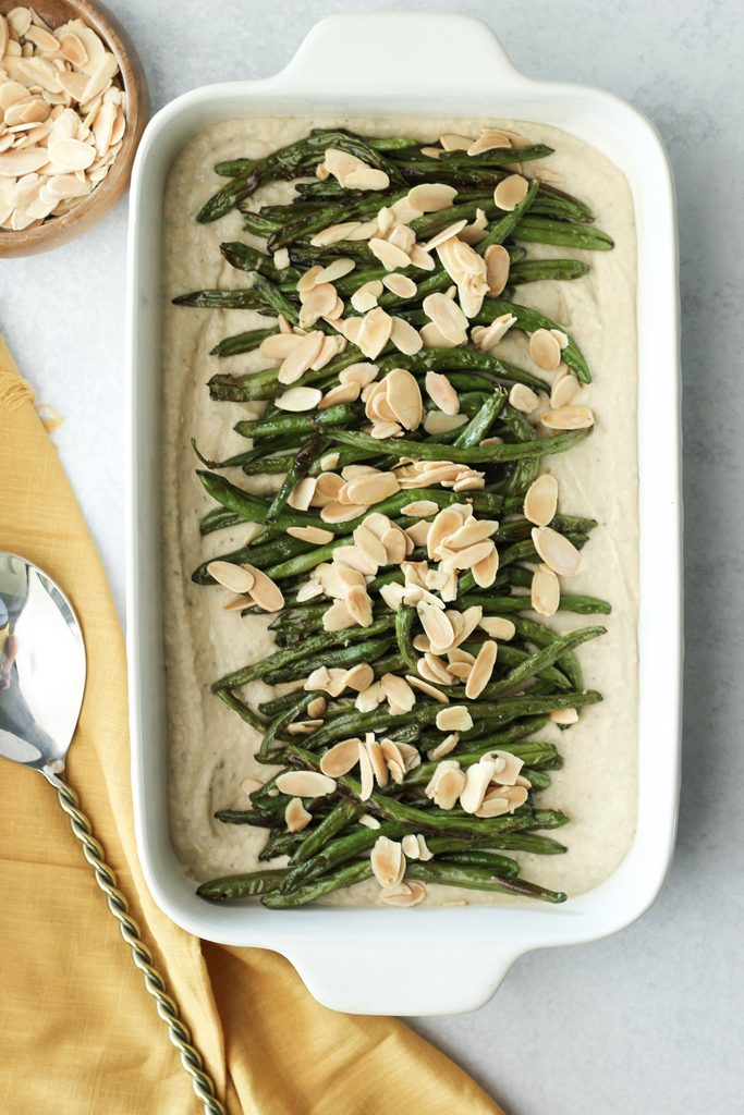 The roasted green beans are in a white casserole dish and are sprinkled with sliced almonds.
