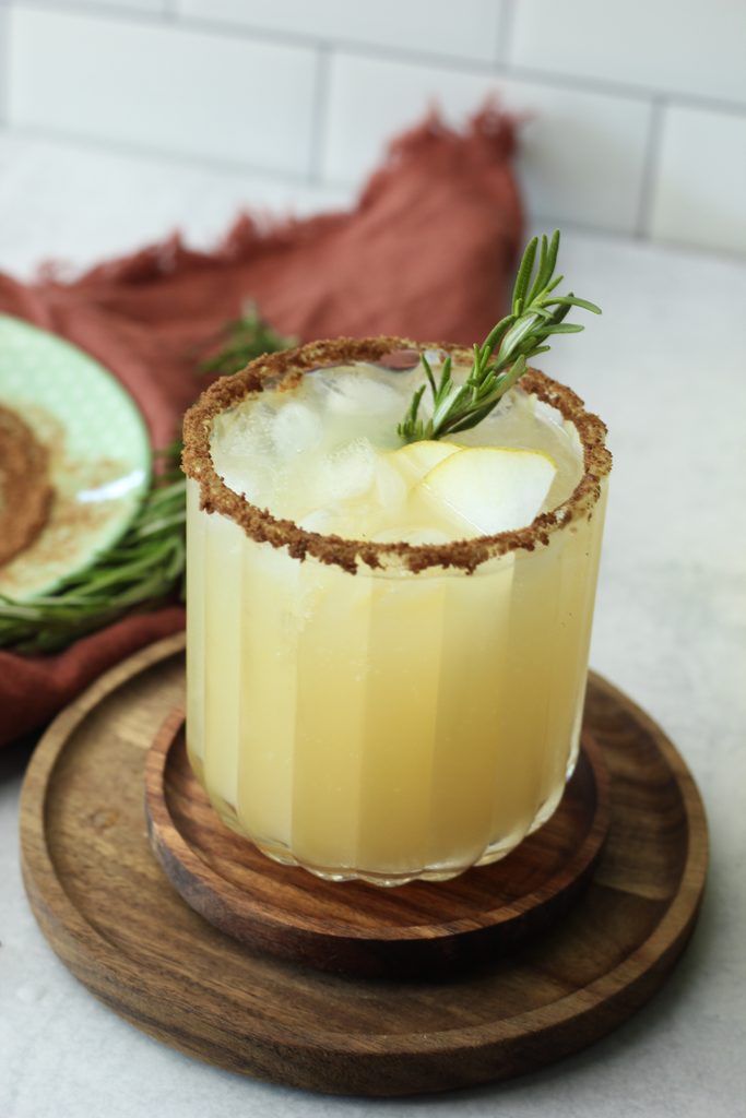 The sparkling pear cocktail has been garnished with a sprig of rosemary and the rim has been covered with cinnamon and sugar.