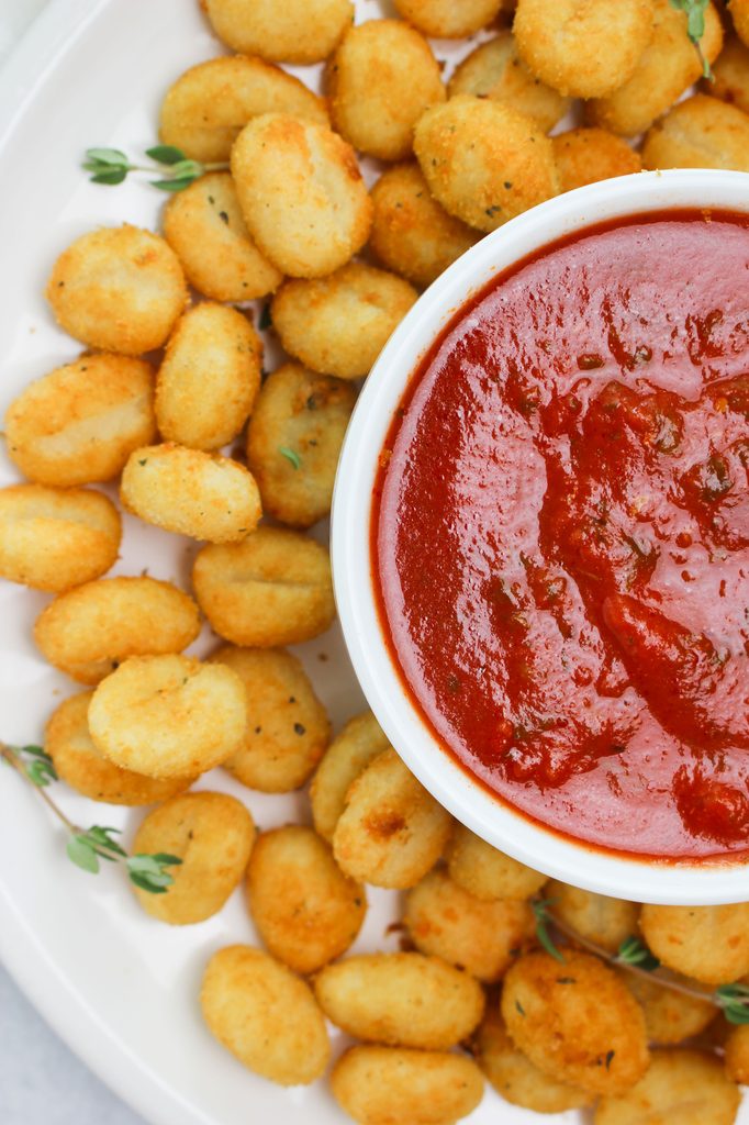 The crispy rosemary garlic air fryer gnocchi are on a white platter with marinara dipping sauce.